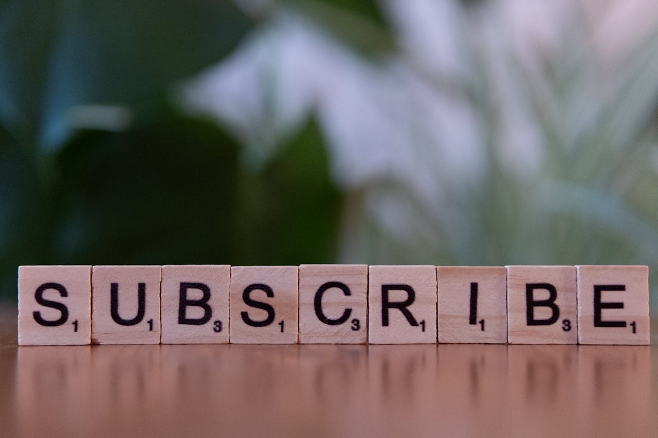 Close-up of the word 'SUBSCRIBE' spelled with wooden letter tiles on a table.