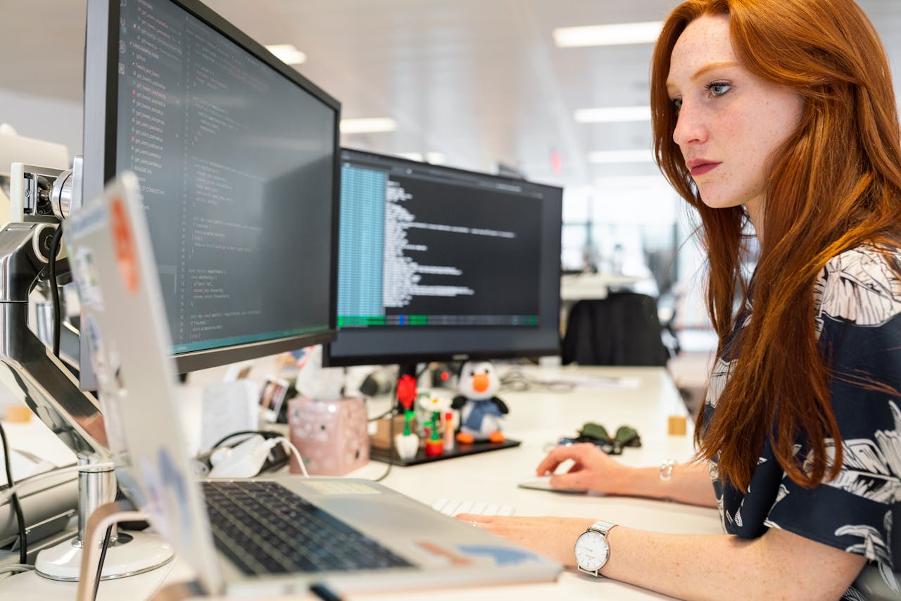 services-img A focused female software engineer coding on dual monitors in a modern office.