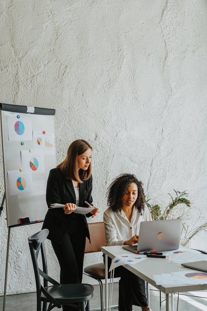 Two businesswomen analyzing graphs on a whiteboard during a meeting.